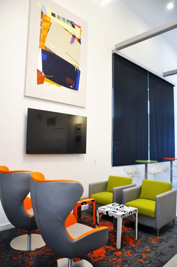 A modern living room with a grey and orange chair, a green couch, and a painting on the wall.